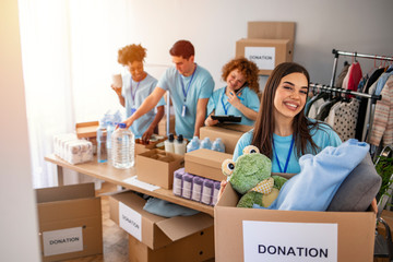 Woman and her colleague working in homeless shelter. Cheerful food drive manager. Happy diverse group of volunteers at food bank. Happy woman volunteers at a food bank