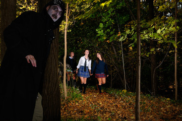 Three happy schoolgirls walking in the woods with a sinister man waiting to ambush them