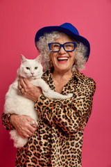 Vertical image of fashionable elderly woman wears hat, leopard outfit, optical glasses, smiles...