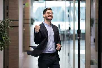 Happy young businessman dancing in office corridor celebrate business success or job promotion,...