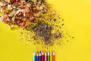 heap of multi-colored shavings and color pencils on a bright yellow background close-up