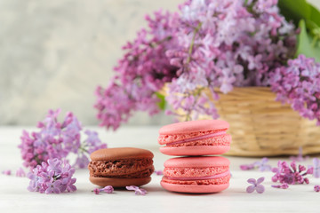 Spring flowers. Twigs of blooming lilac in a wicker basket and macaroon cake on a light concrete background