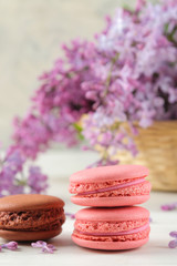 Fototapeta na wymiar Spring flowers. Twigs of blooming lilac in a wicker basket and macaroon cake on a light concrete background