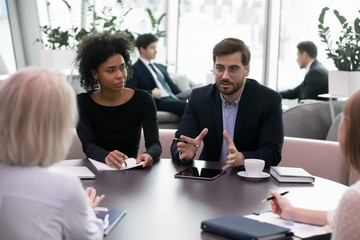 Multiracial businesspeople talk brainstorm about financial project or plans together, concentrated diverse colleagues coworkers cooperate discuss strategy at meeting in office, collaboration concept