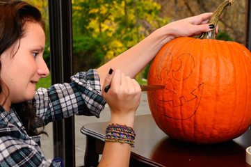 Young teenage girl struggling to cut a face pattern onto a pumpkin for Halloween