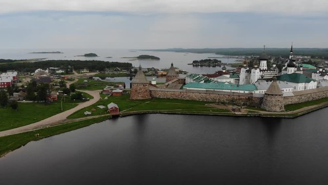 Smooth cinematic flyby of the Solovetsky monastery from the side of the Holy lake with a view of the White sea on a cloudy day with soft lighting. 