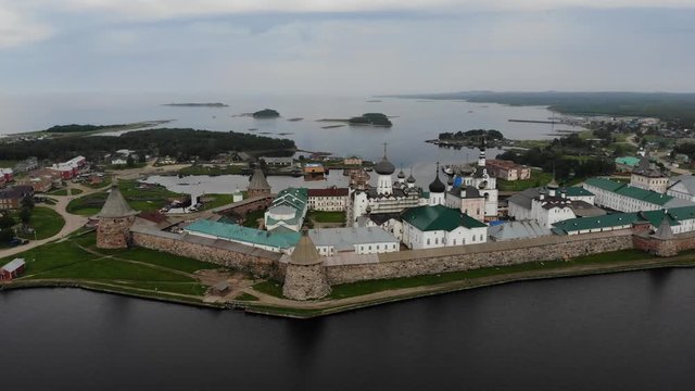 Smooth cinematic flyby of the Solovetsky monastery from the side of the Holy lake with a view of the White sea on a cloudy day with soft lighting. 