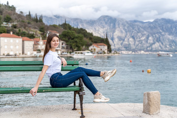 Woman in orange hoodie stands by the sea in city Perast on the background in Montenegro