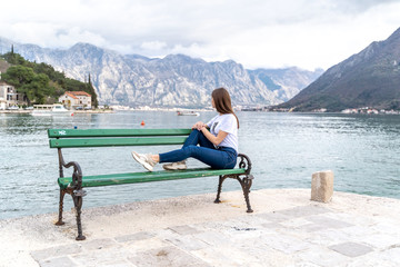 Fototapeta premium Woman in orange hoodie stands by the sea in city Perast on the background in Montenegro