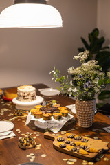 Decorated Birthday table with different cupcakes, muffins, cake and madeleines with flowers and confetti.