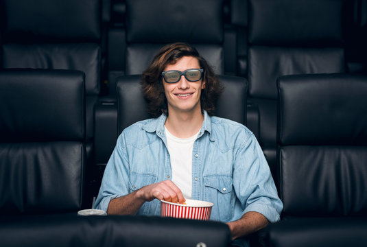 Handsome young man with popcorn and 3D glasses in cinema - Powered by Adobe