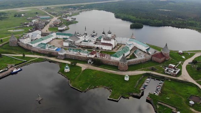 Smooth cinematic flyby of the Solovetsky monastery from the side of the White sea with a view of the Saint Lake on a cloudy day with soft lighting.