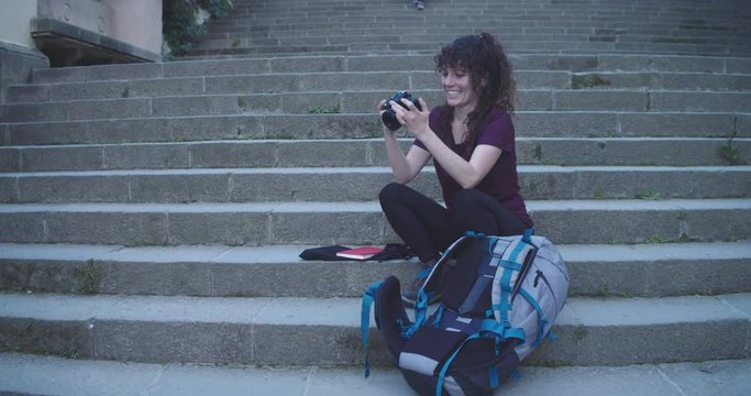 Smiling traveler woman with a backpack looking at the photos of a reflex camera. Traveler, adventurer