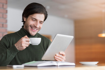 Happy young man reading emails while drinking coffe at cafe