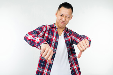 Asian guy in a checkered shirt wide open shows dislike finger down on an isolated white studio...