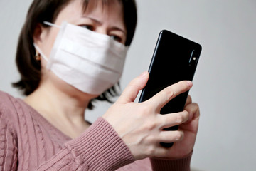 Woman in medical mask using smartphone, close-up mobile phone in female hands. Concept of illness, fever, cold and flu, search for coronavirus symptoms