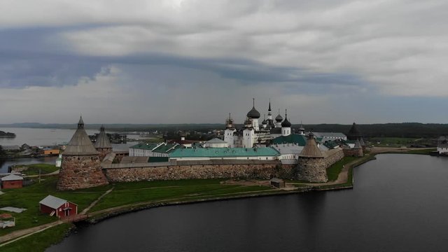 Smooth cinematic flyby of the Solovetsky monastery from the side of the Holy lake with a view of the White sea on a cloudy day with soft lighting. 