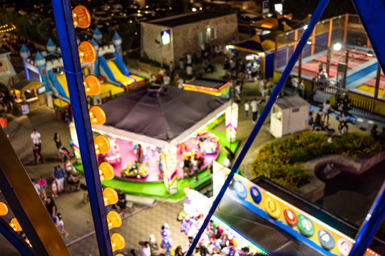 Families and children enjoy the rides, at night, in the summer in Torre Vado. Fun place for tourists, with rides. In Italy, Puglia, Lecce, Salento. Blur photo taken from the top of the Ferris wheel.