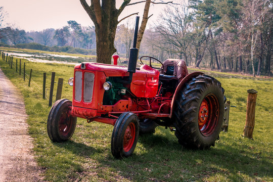 Old red vintage tractor on the land in the beautiful landscape of Drenthe near Havelte