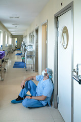 Male nurse sitting in hospital hallway because he is exhausted