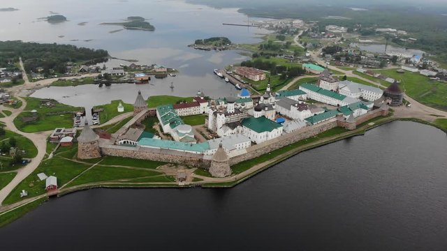 Smooth cinematic flyby of the Solovetsky monastery from the south side with a view of the White sea, Saint Lake and nearby village on a cloudy day with soft lighting. 