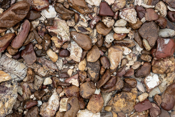 Multicolor stones of different shapes and size. Small rocks on beach sand close up.
