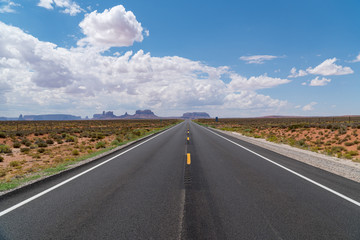 Endless straight road in America on a sunny day with a few clouds