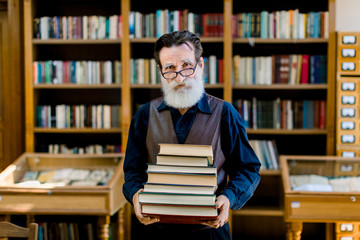 Portrait of positive smart old bearded man in dark shirt and leather vest, library worker, teacher,...