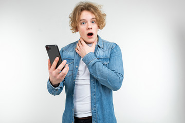 blond man with wavy white hair and surprise on his face with a smartphone in his hands on a white studio background