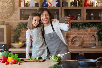 Happy father and little daughter taking selfie on smartphone in kitchen