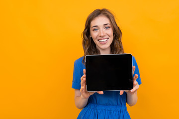 girl in a blue dress with a tablet with a blank mockup on a yellow and orange background with copy space