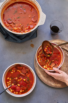 Overhead image of female hand serving tomato soup with chickpeas, chorizo sausage and parsley