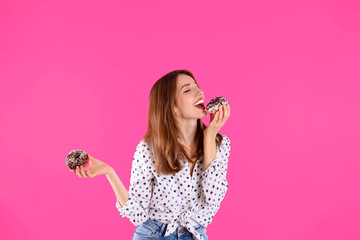 Beautiful young woman with donuts on light pink background