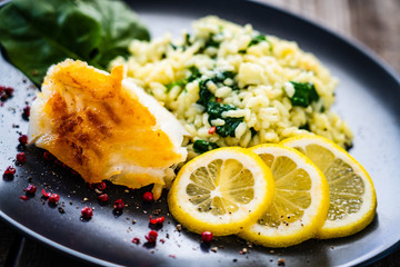 Risotto with fried cod on wooden background
