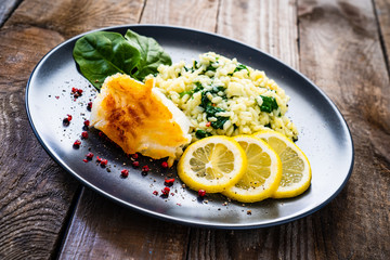 Risotto with fried cod on wooden background