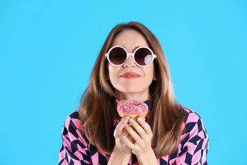 Beautiful young woman wearing sunglasses with donut on light blue background