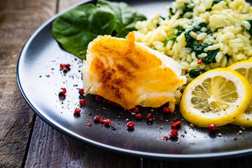 Risotto with fried cod on wooden background