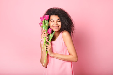 Young african woman with flowers on pink background. Women's day concept