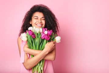 Young african woman with flowers on pink background. Women's day concept