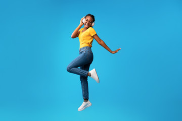 Fototapeta na wymiar African Lady In Earphones Jumping Having Fun In Studio