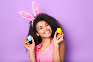 Young african woman with rabbit ears and eggs against purple background. Easter concept