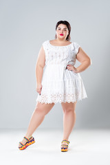 Plus size fashion model in white dress, fat woman on gray background, body positive concept