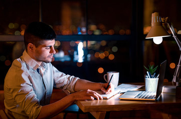 Business Guy Taking Notes Working Overnight Sitting In Office, Low-Light