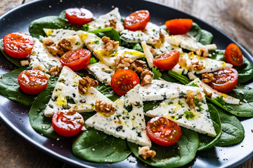 Fresh salad - blue cheese, cherry tomatoes, spinach, walnuts on wooden background