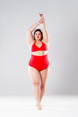 Plus size fashion model in red swimsuit, fat woman in lingerie on gray background