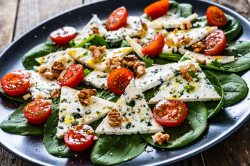 Fresh salad - blue cheese, cherry tomatoes, spinach, walnuts on wooden background