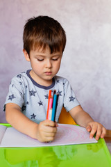 Little boy drawing with color pencils. There are many colored pencils in the boy's hands. Small boy draws at the table.