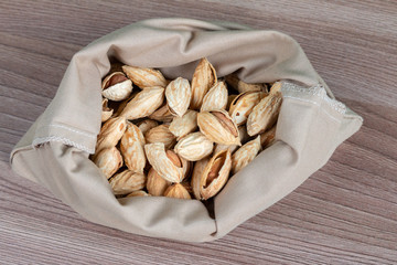 Unpeeled raw almonds in a handmade textile bag, organic and healthy food concept. Space for text, wooden table 