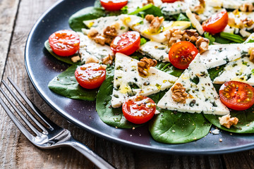 Fresh salad - blue cheese, cherry tomatoes, spinach, walnuts on wooden background