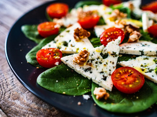 Fresh salad - blue cheese, cherry tomatoes, spinach, walnuts on wooden background